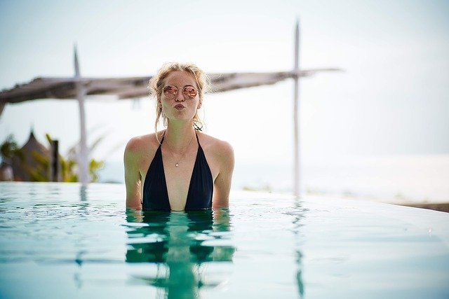 ragazza bionda in piscina con costume nero e occhiali da sole