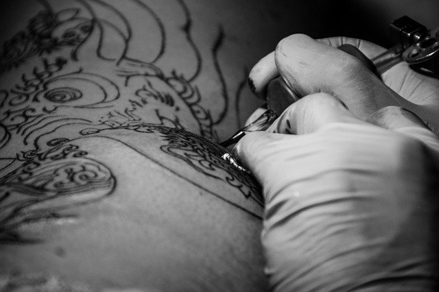 mani con guanti e macchinetta per tatuare su corpo nudo
