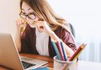 ragazza con occhiali e capelli lunghi tiene matita in bocca davanti a laptop