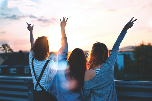 ragazze di schiena alzano le mani al cielo al tramonto