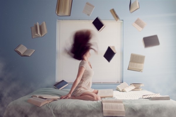 ragazza su letto e libri che volano