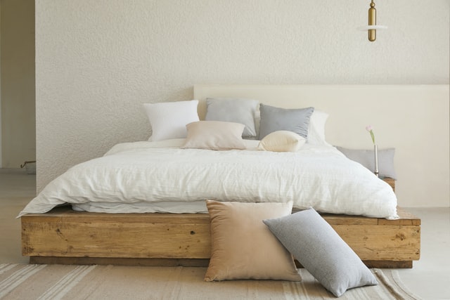 letto con struttura di legno lenzuola bianche e cuscini dai colori chiari