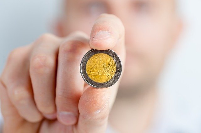 uomo tiene moneta da due euro tra le dita