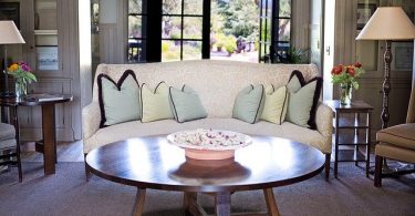 tavolino rotondo di legno davanti a divano bianco con cuscini azzurri