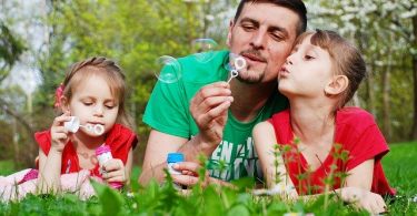 padre fa bolle di sapone con figlie in giardino