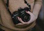ragazza con maglione marrone tiene macchina fotografica