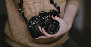 ragazza con maglione marrone tiene macchina fotografica