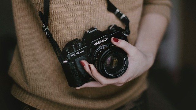 ragazza con maglione marrone tiene macchina fotografica