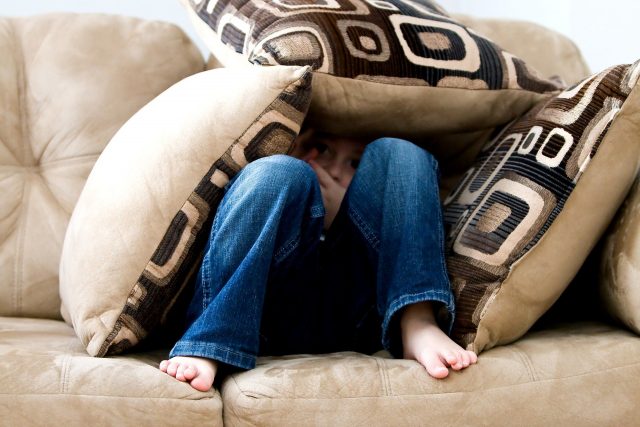 bambino seduto sotto pila di cuscini sul divano