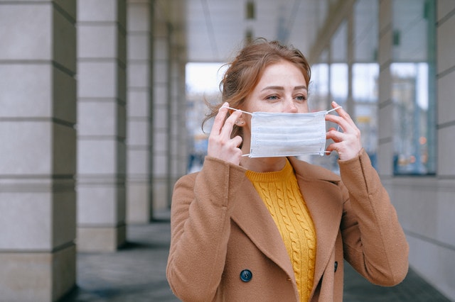 ragazza bionda con cappotto marrone mette mascherina