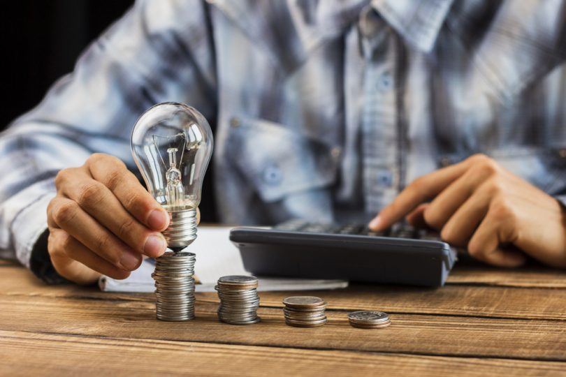uomo tiene una lampadina in mano su un tavolo con monete e una calcolatrice