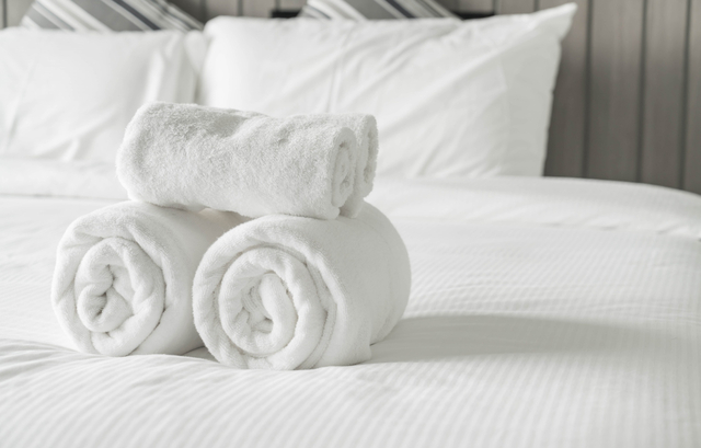 asciugamani bianchi arrotolati su letto con lenzuola bianche