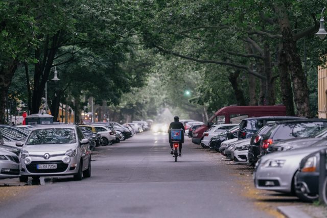 persona in bicicletta su strada con auto parcheggiate