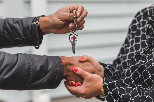 primo piano su stretta di mano tra uomo e donna con chiavi di una casa