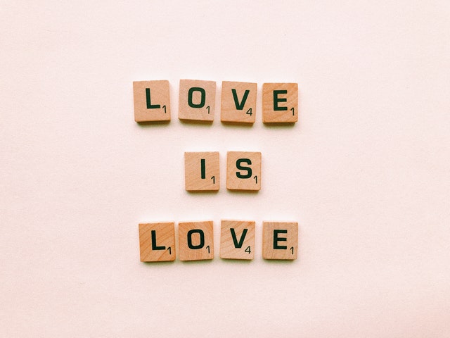 scritta love is love con quadratini di legno su sfondo rosa