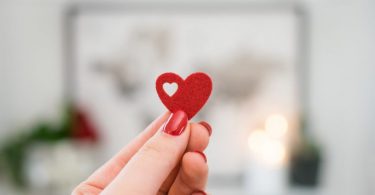 primo piano su mano di ragazza con smalto rosso che tiene un cuore di feltro