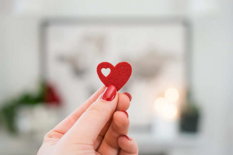 primo piano su mano di ragazza con smalto rosso che tiene un cuore di feltro