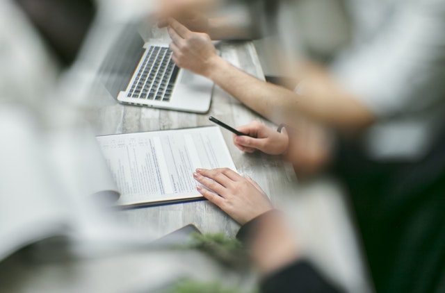 primo piano su 4 mani a una scrivania con fogli e pc